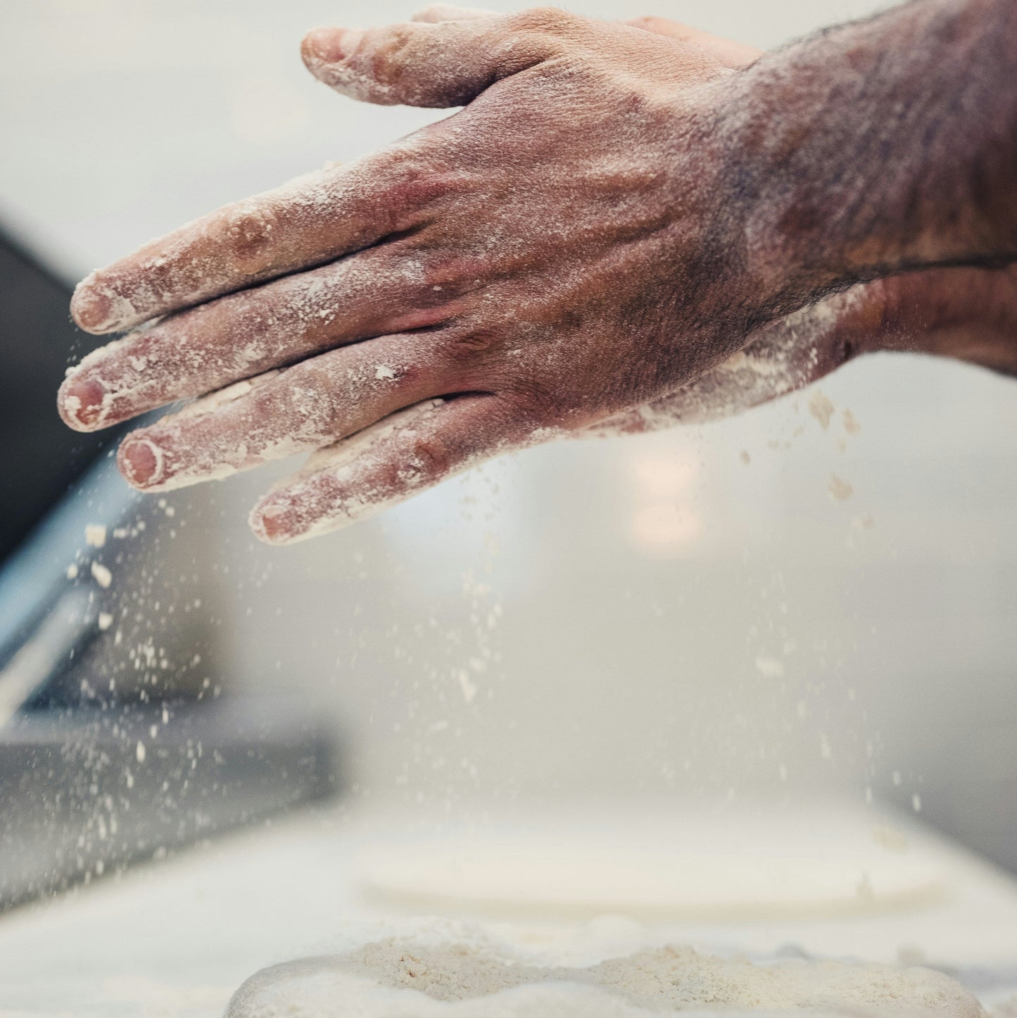 Hand with flour dusting over a dough on a floured surface