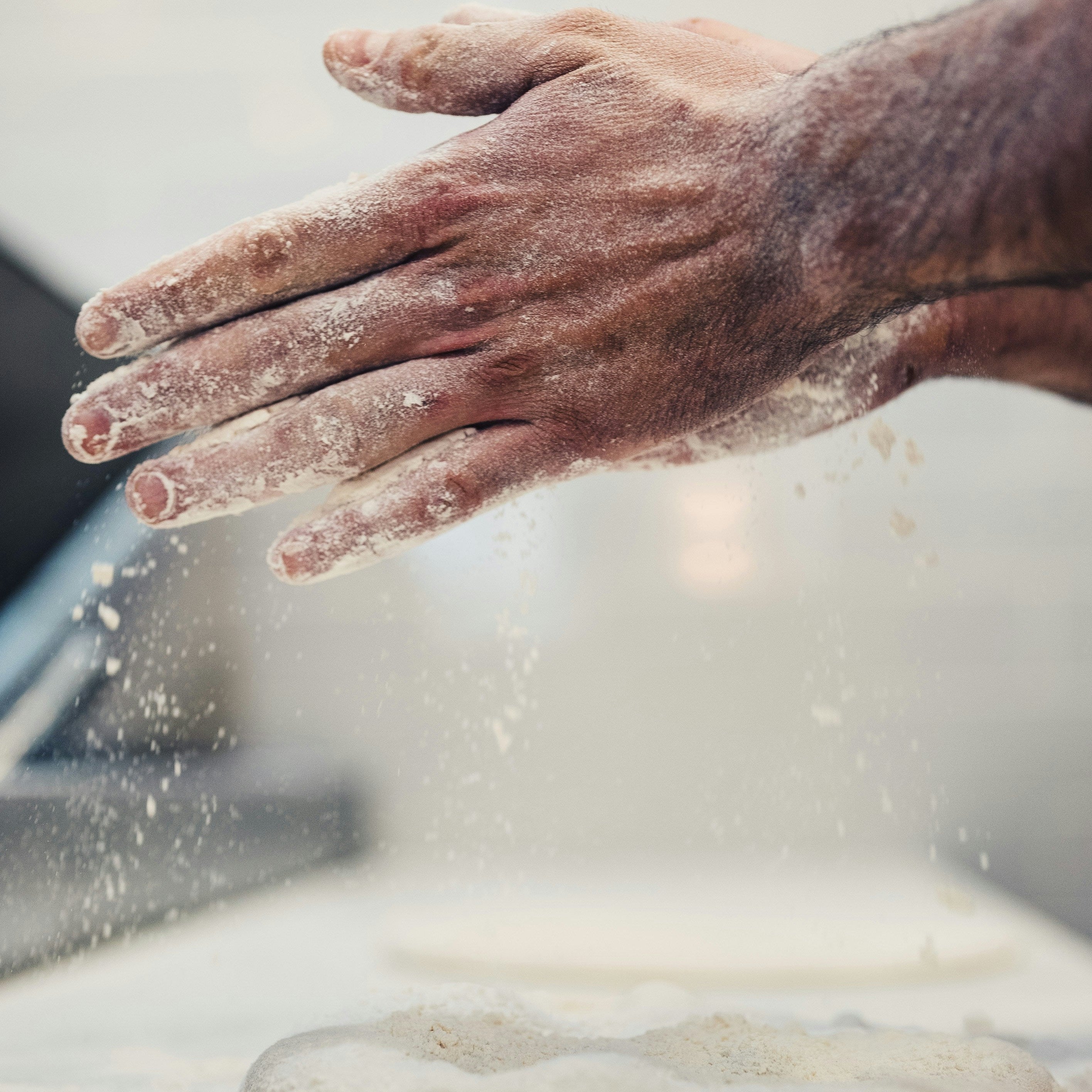 Hand with flour dusting over a dough on a floured surface